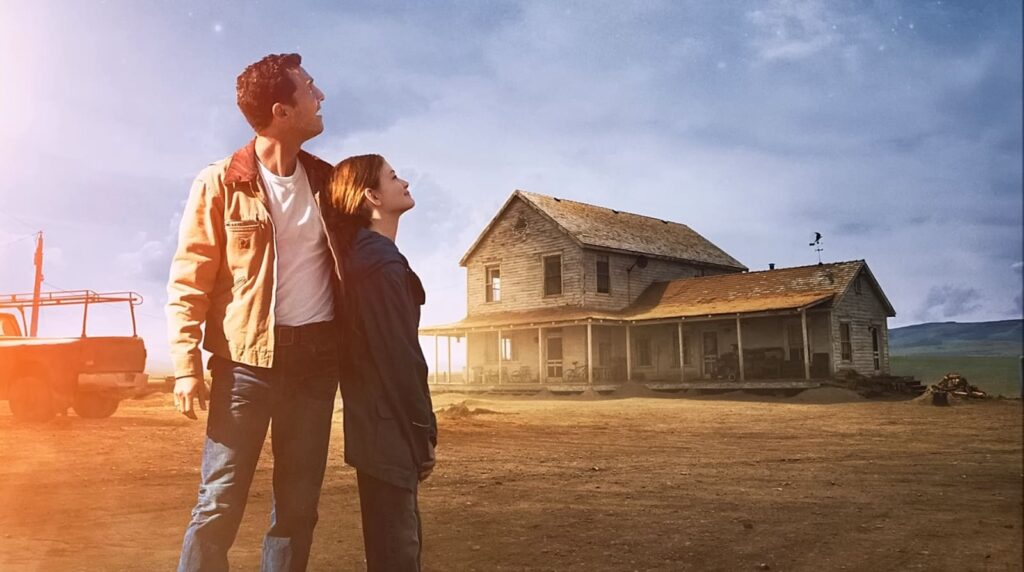 Two people gaze skyward by a farmhouse with a vintage truck nearby